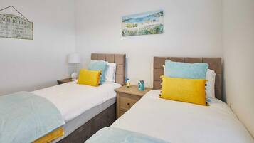 Una habitación con dos camas, cada una con cabecera, mesita de noche, lámpara y un pequeño objeto decorativo.