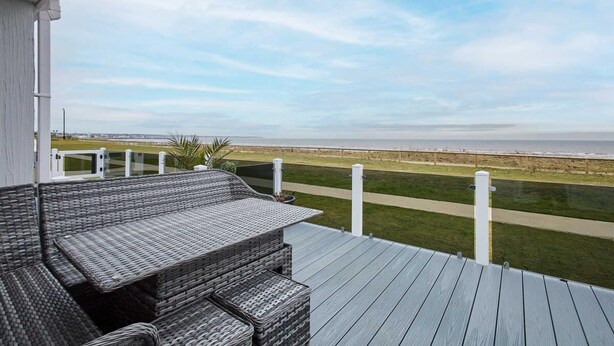 A deck with wicker furniture overlooking a grassy area and a distant view of the beach. - Host Stay Sea View Road (Bridlington)