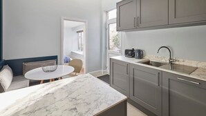 A compact kitchen with grey cabinets, a marble countertop, and a small dining area with a round table and chairs. - Host Stay Mollymac Ground Floor (Saltburn-by-the-Sea)