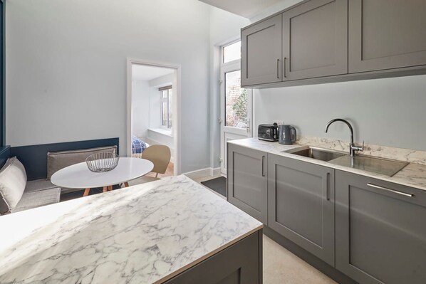 A compact kitchen with grey cabinets, a marble countertop, and a small dining area with a round table and chairs. - Host Stay Mollymac Ground Floor (Saltburn-by-the-Sea)