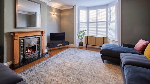 A living room with a fireplace, a television, a large window, and a dark-colored sofa. - Host Stay Mollymac Ground Floor (Saltburn-by-the-Sea)