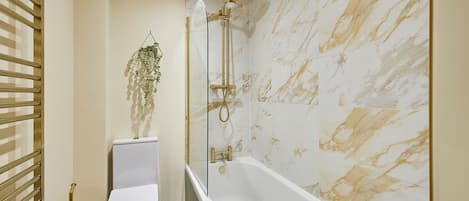 A bathroom with a white toilet, a glass-enclosed shower with gold fixtures, and marble-patterned walls.