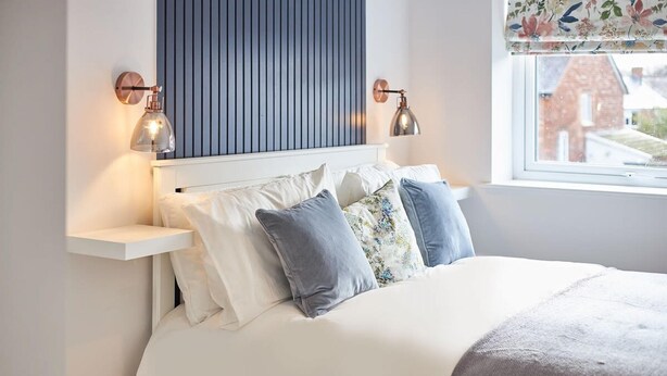 Une chambre à coucher avec un lit, des oreillers, une tête de lit et des lampes fixées au mur.