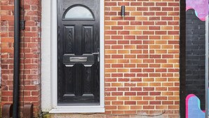 Une porte noire surmontée d’une fenêtre blanche, le tout intégré dans un mur de briques agrémenté d’un élément décoratif noir et rose sur le côté droit.