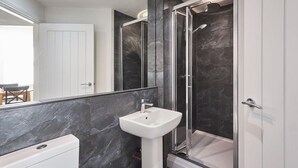 Une salle de bain moderne avec un lavabo blanc, une douche en verre et des murs recouverts de marbre foncé.