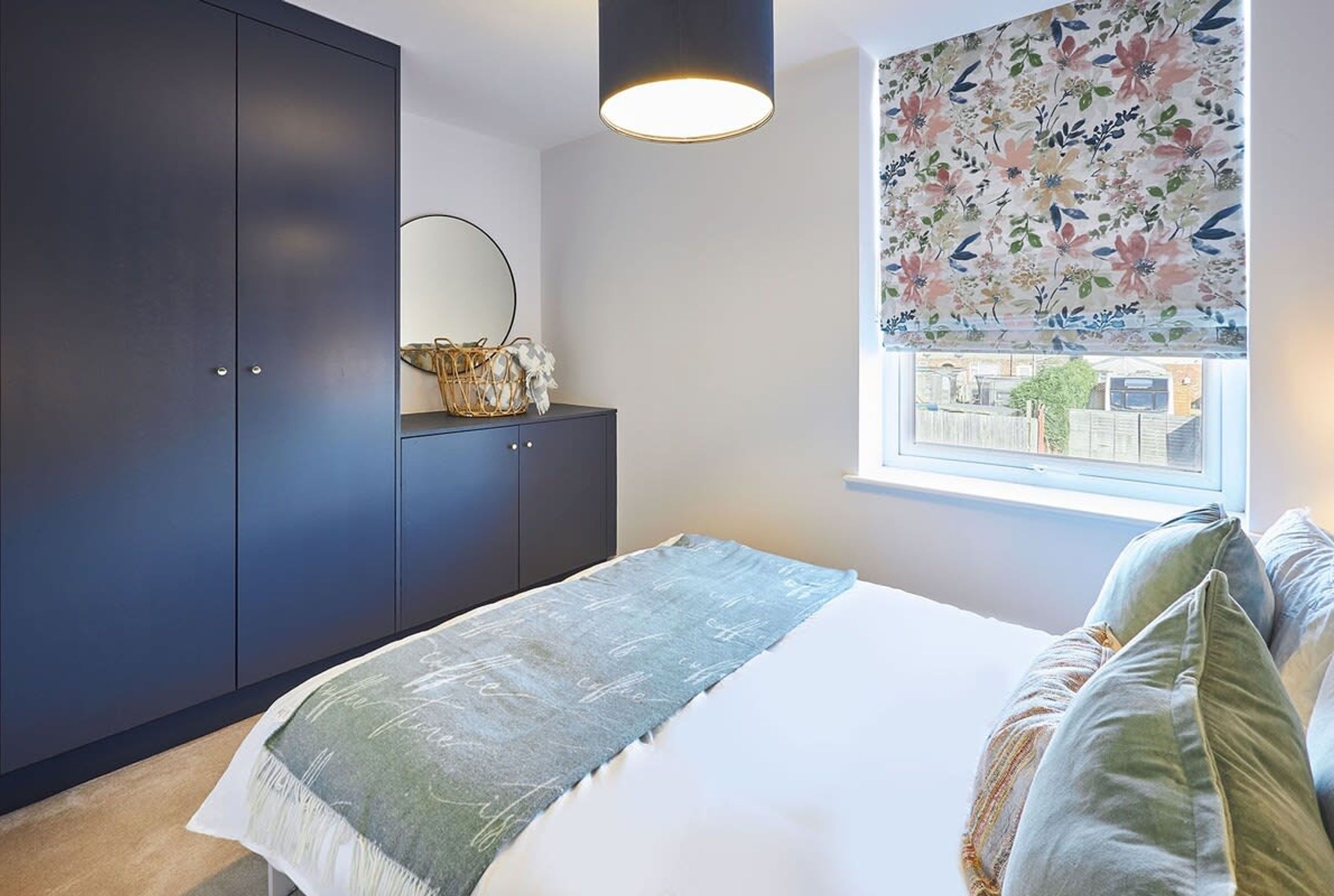 A bedroom with a bed, dark wardrobe, bedside table, and a window with a floral view.