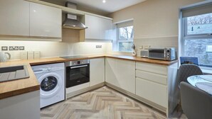 A modern kitchen with built-in appliances, a washing machine, and a dining area with a view. - Host Stay Column Mews (Alnwick)