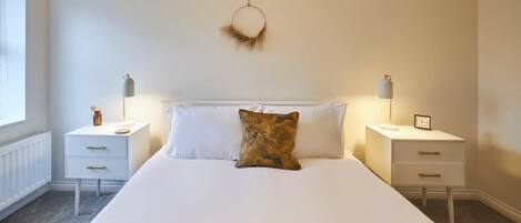 A bedroom with a large bed, two bedside tables, a wall-mounted decoration, and a window.