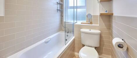 A bathroom with a bathtub, toilet, and a window.