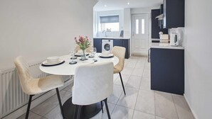 A modern kitchen with a built-in washing machine, a dining area with a round table and chairs, and a small island with a kettle. - Host Stay Marsden Beach House (South Shields)