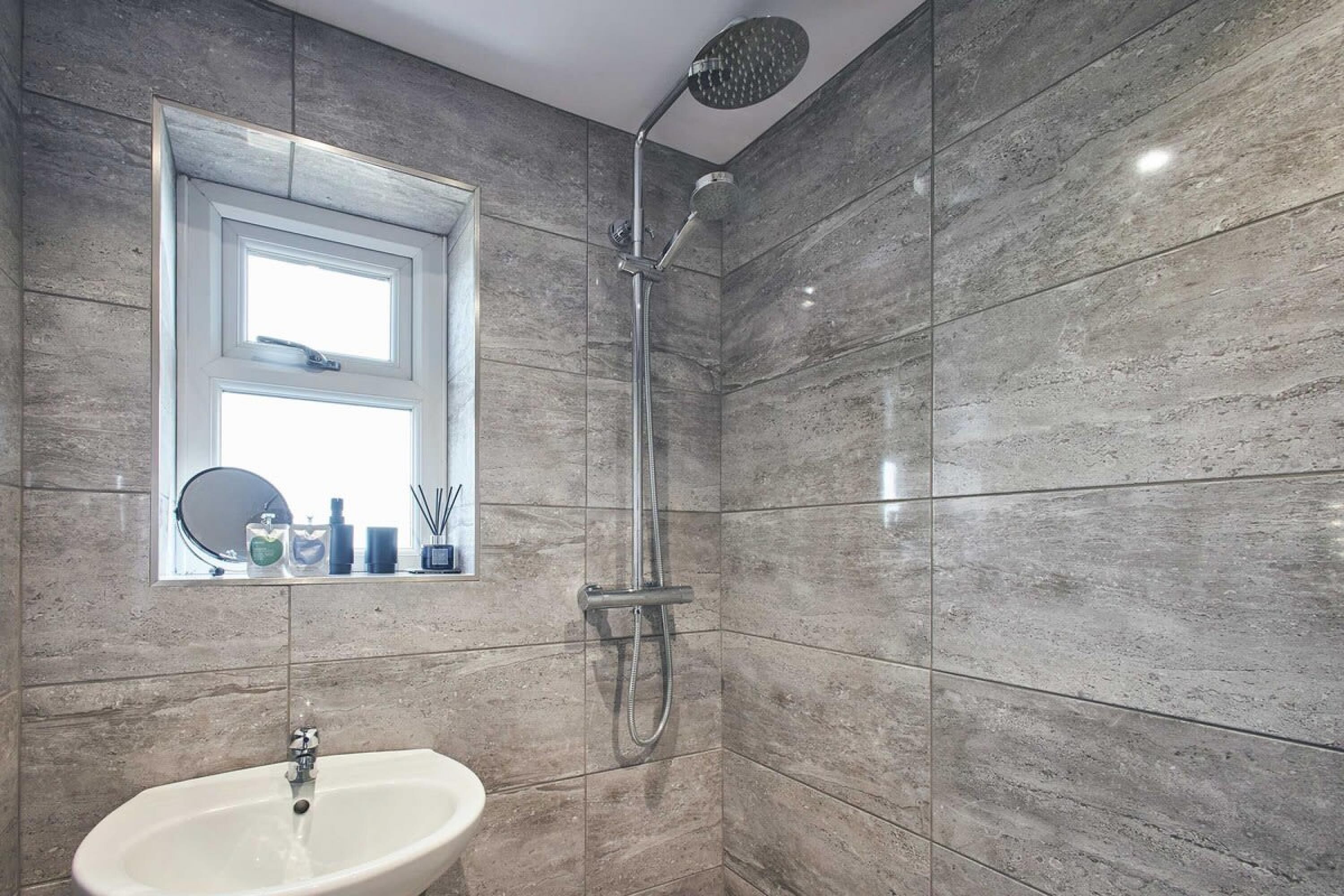 A bathroom with a sink, a window with a mirror, and a shower.