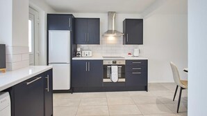 A compact kitchen with dark cabinets, a white refrigerator, a built-in oven, and a coffee maker. - Host Stay Marsden Beach House (South Shields)