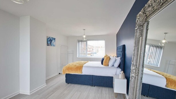 A modern bedroom with a large bed, a white bedside table, a mirror, and a window with blinds. - Host Stay Marsden Beach House (South Shields)