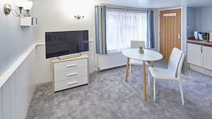 Ein kleines Zimmer mit Fernseher, Esstisch, Stuhl und Schrank.