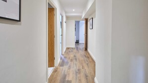 Un pasillo con piso de madera, paredes blancas y cuadros enmarcados a la derecha.