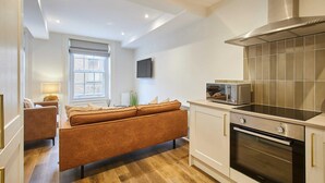 Una cocina moderna con horno empotrado y microondas, suelo de madera, y un sofá en la zona de estar contigua.