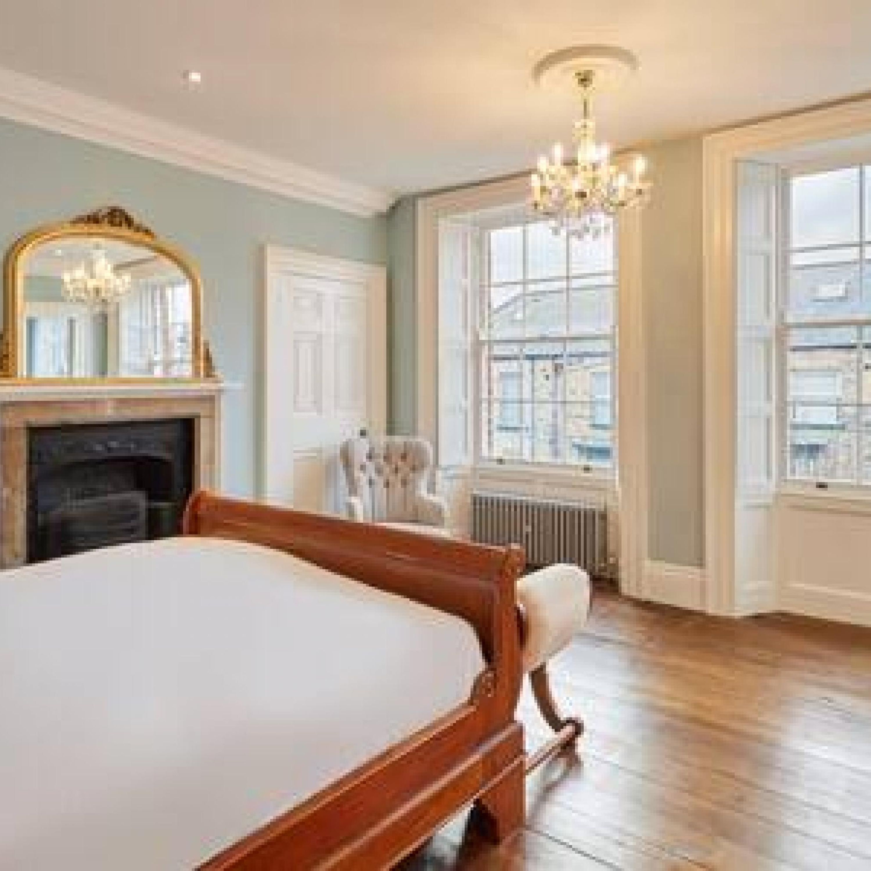 A spacious bedroom with a large bed, a fireplace, a chandelier, and large windows with a city view.