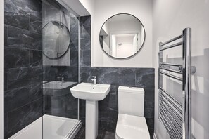 A modern bathroom with a glass-enclosed shower, a pedestal sink, a toilet, and a wall-mounted mirror.