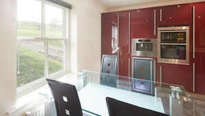 A modern kitchen with red cabinets, stainless steel appliances, and a glass dining table.