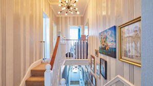 A grand staircase with a white balustrade, a chandelier, and framed artwork on the walls. - Host Stay The Beach House (Redcar)