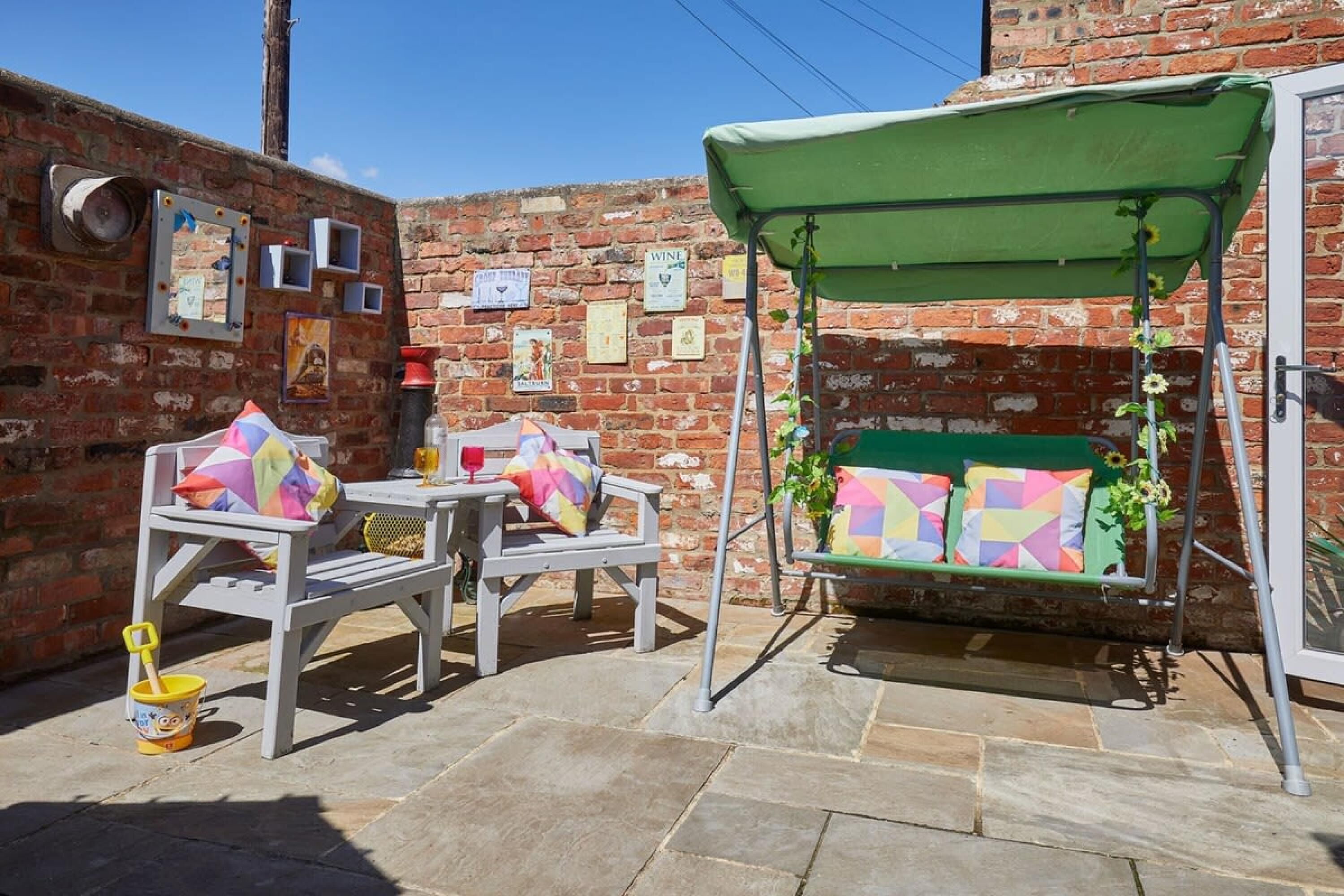 A patio with two white chairs, a small table, and a green swing.