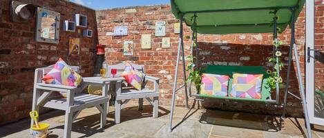 A patio with two white chairs, a small table, and a green swing.