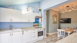 A modern kitchen with white cabinets, a built-in oven, and a dining area with a wooden table and chairs. - Host Stay The Beach House (Redcar)