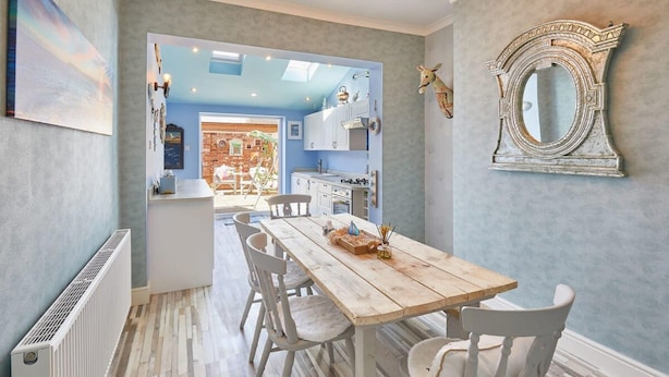 A dining area with a wooden table and white chairs, a white radiator, and a decorative mirror on the wall. - Host Stay The Beach House (Redcar)