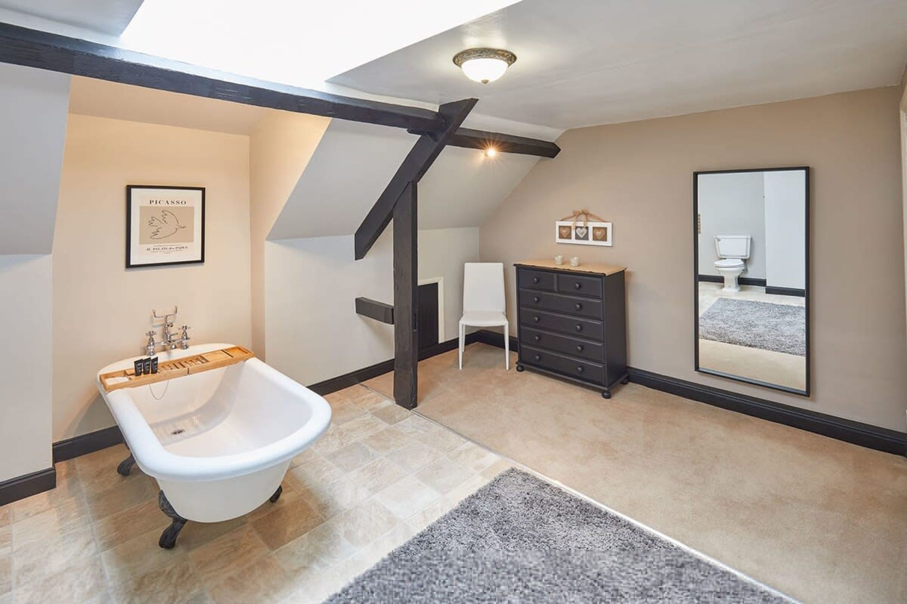 A bathroom with a freestanding bathtub, a vanity with a mirror, and a framed artwork on the wall.