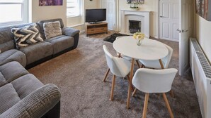 Ein Wohnzimmer mit Sofa, Fernseher, Kamin und einem Esstisch mit Stühlen.