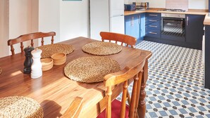 A modern kitchen with a dining area, featuring a wooden table, woven placemats, and a tiled floor. - Host Stay Hideaway (Morpeth)