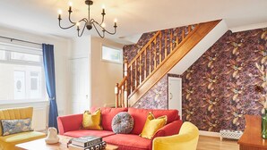 A living room with a red sofa, yellow armchair, and a wooden coffee table. A staircase with a floral wallpapered wall leads to another level. - Host Stay Hideaway (Morpeth)