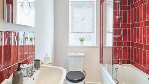 A bathroom with a white sink, black toilet, and a bathtub with red tiles. - Host Stay Hideaway (Morpeth)