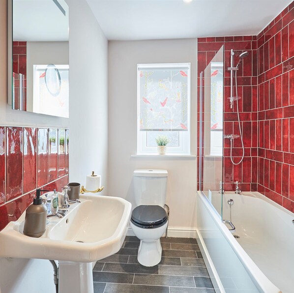 Une salle de bain avec un lavabo blanc, des toilettes noires et une baignoire dont les carreaux sont rouges.