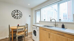 A compact kitchen with a washing machine, a sink, and a window with blinds. - Host Stay Station View (Saltburn-by-the-Sea)