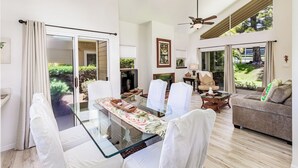 A spacious living room with a glass dining table, white chairs, a sofa, and a ceiling fan.