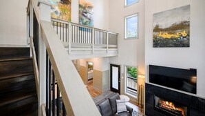 A spacious living area with a staircase, a fireplace, and artwork on the walls.