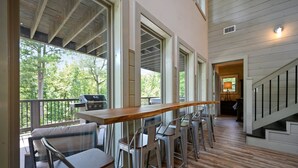 A bar area with high ceilings and large windows, a wooden deck, and a staircase leading to an upper level.