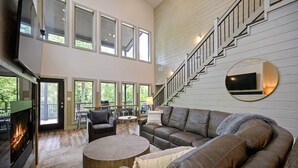 A spacious living room with a fireplace, leather sofas, a round coffee table, and a staircase with a TV mounted on the wall.