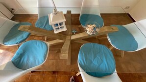 A dining area with a glass table surrounded by four chairs with blue cushions, a small wooden side table with a lamp, and a decorative bowl on the table. - Villa Lisa holiday home (Città del Mare-perla del Golfo)