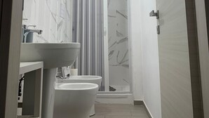 A modern bathroom with a toilet, bidet, and a shower with a striped curtain. - Il Buon Risveglio Agropoli (Agropoli)