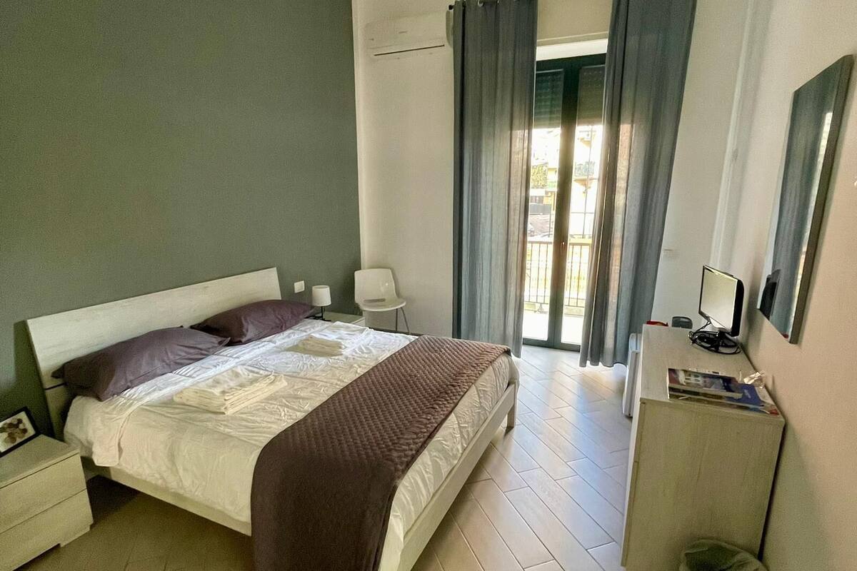 A bedroom with a bed, bedside tables, a chair, a desk, a computer, and a window with curtains.