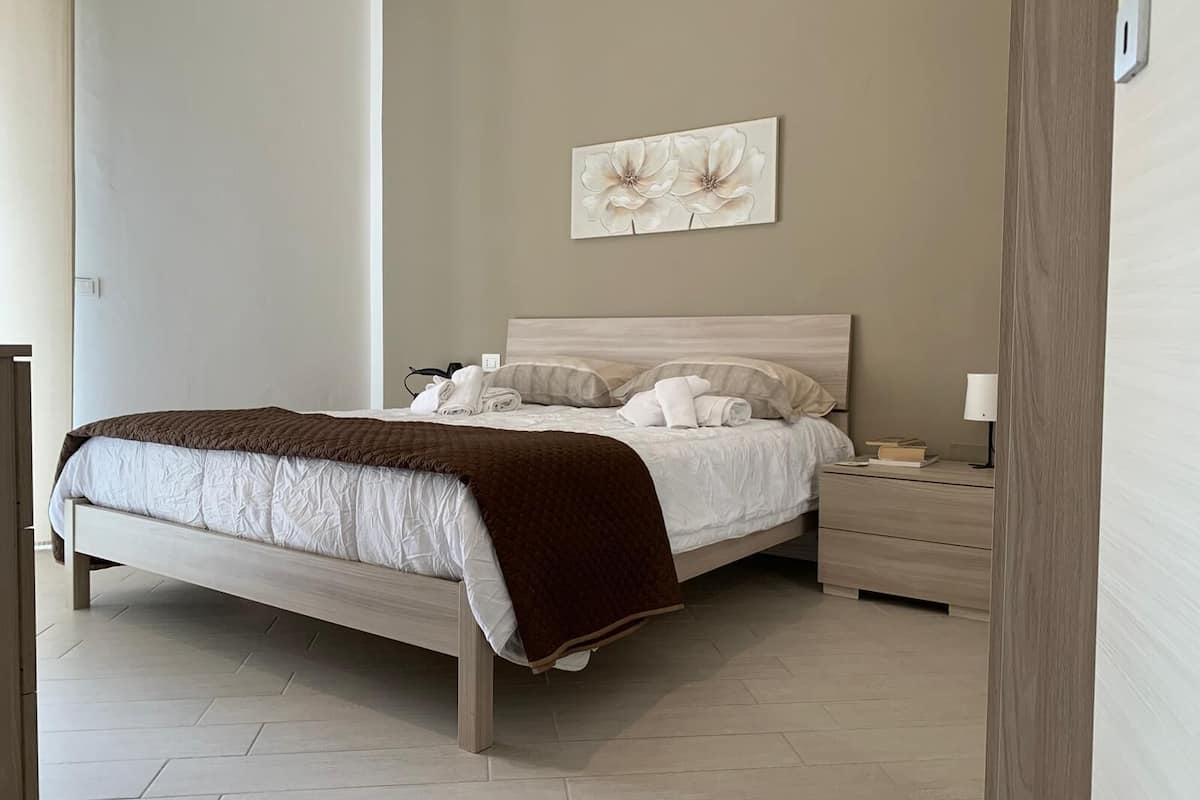 A neatly arranged bedroom with a bed, bedside tables, and a wall-mounted artwork.