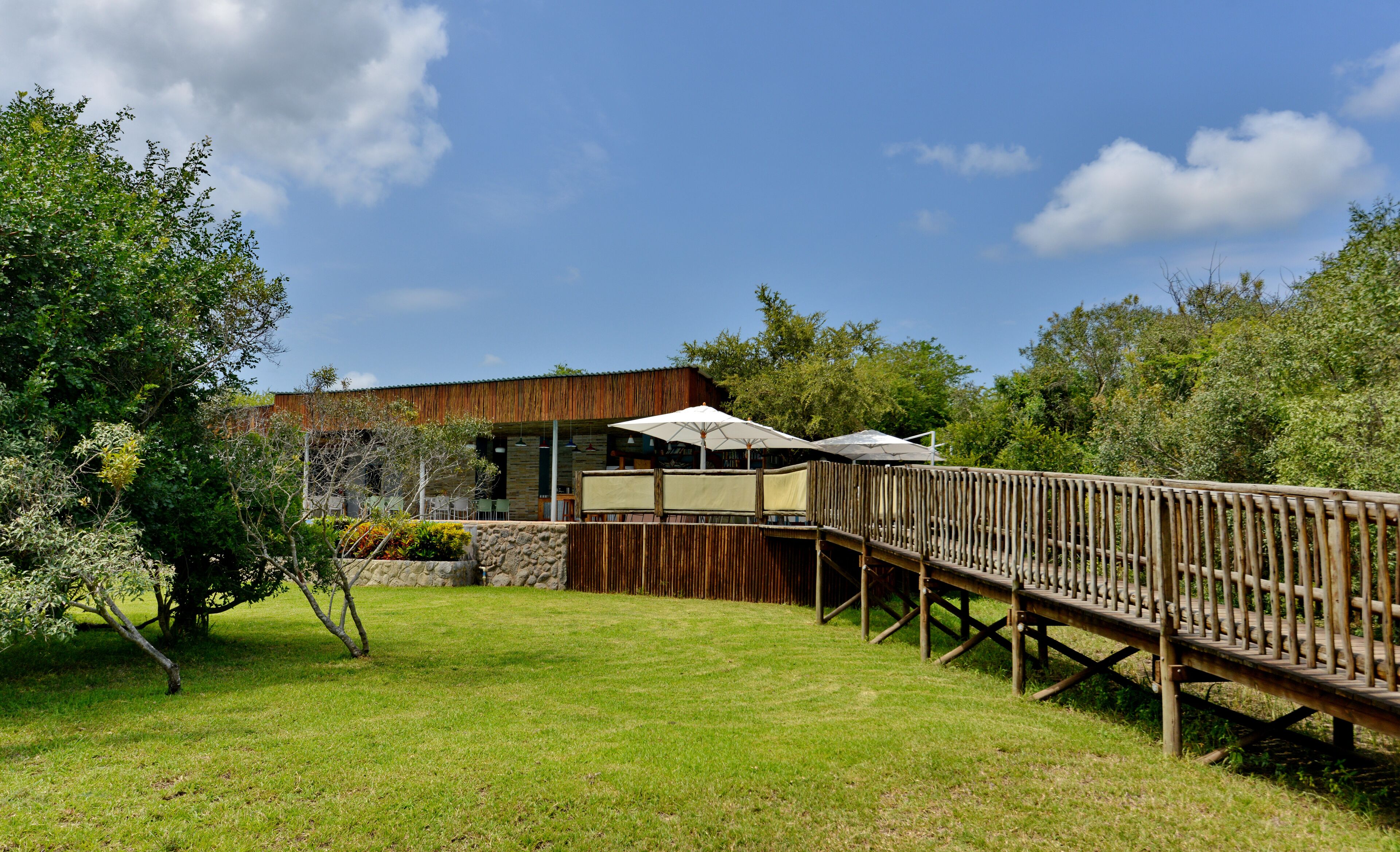 A wooden deck leading to a stone building with outdoor seating and umbrellas.