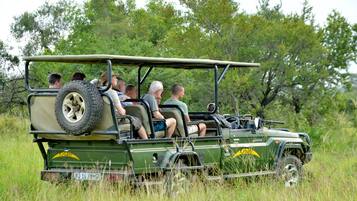 A safari vehicle with passengers, surrounded by tall grass and trees.