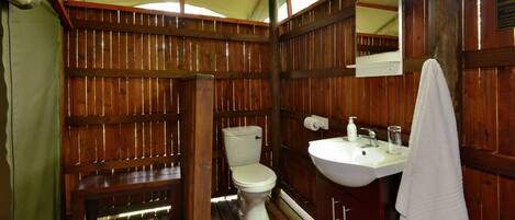 A wooden cabin-style bathroom with a toilet, sink, and bench.