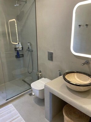 A modern bathroom with a glass shower enclosure, a toilet, a sink with a marble basin, and a mirror with LED lighting. - Mykonian Ocean Dream House Agios Sostis (Mykonos)