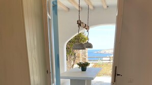 Une chambre à coucher avec un lit, un banc et une vue sur la mer, visible par une porte ouverte.
