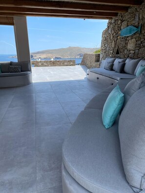 Un'area salotto all'aperto riparata, con un muro in pietra e vista sul mare.