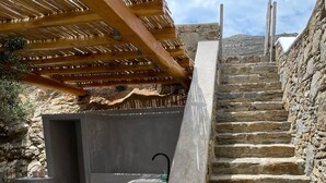 Un escalier en pierre mène à un espace extérieur abrité, où se trouvent un banc en béton et un évier.